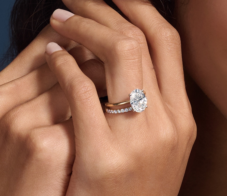 Close-up of a hand wearing a yellow gold engagement ring with an oval-cut diamond center stone, paired with a matching yellow gold wedding band featuring a row of round diamonds.