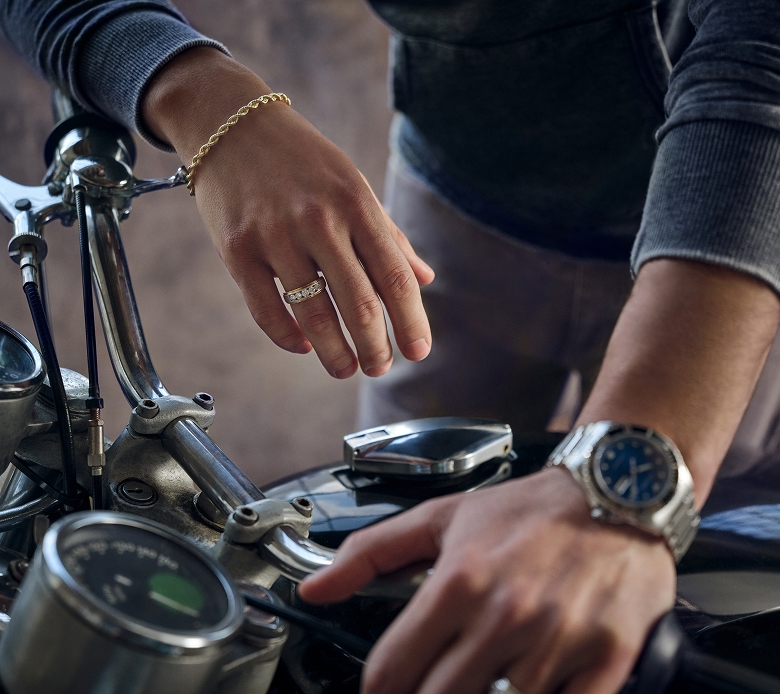 Image of male arms with a watch and chain bracelet draped over the handlebars of a motorcycle. Shop the fathers day sale.