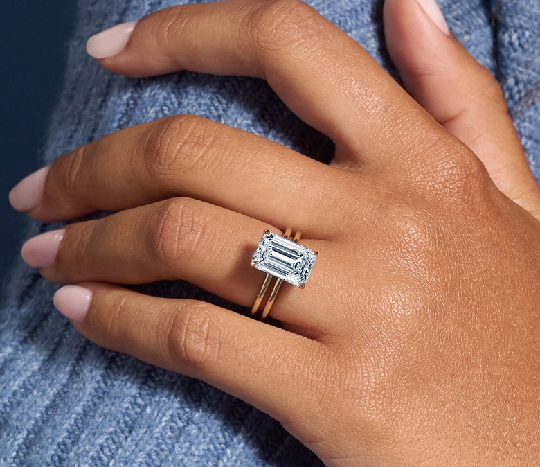 A Helzberg solitaire engagement ring with an emerald cut diamond and a yellow gold double band.