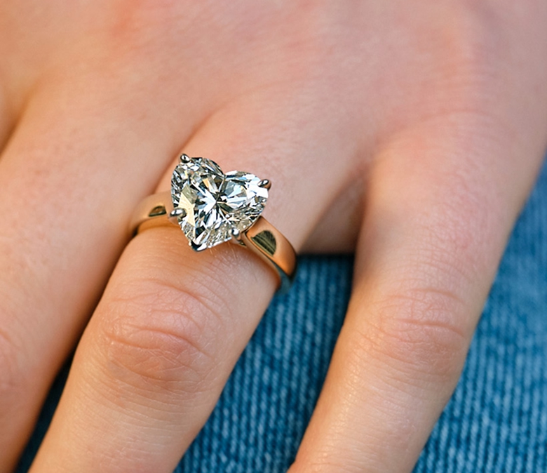Close-up of a hand wearing a yellow gold engagement ring featuring a heart-shaped diamond center stone.