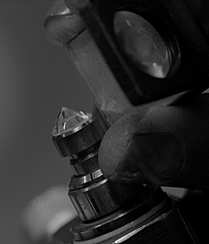 Close-up of a diamond held in a metal clamp during the cutting or inspection process, with a jeweler&rsquo;s loupe positioned nearby.