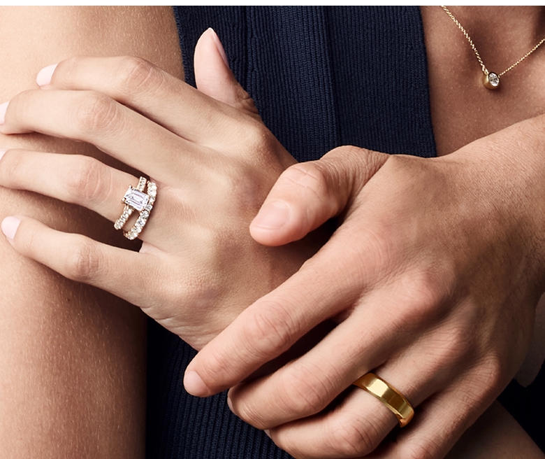 Image of a female hand wearing a moissanite engagement ring and wedding band being held by male hand wearing a yellow gold wedding band. What gives moissanite its sparkle?