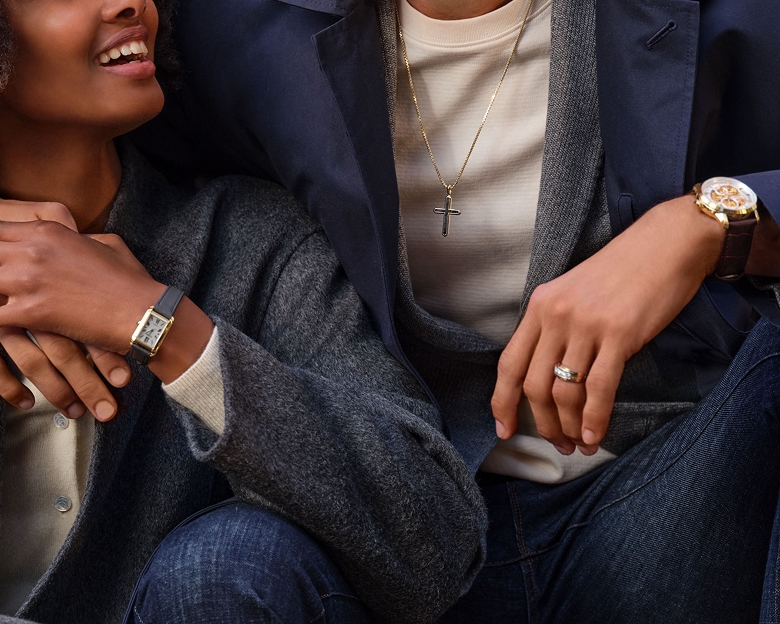 An image of a mans arm around a woman. Both sitting on an outdoor concrete staircase and both of their wrists feature a watch.