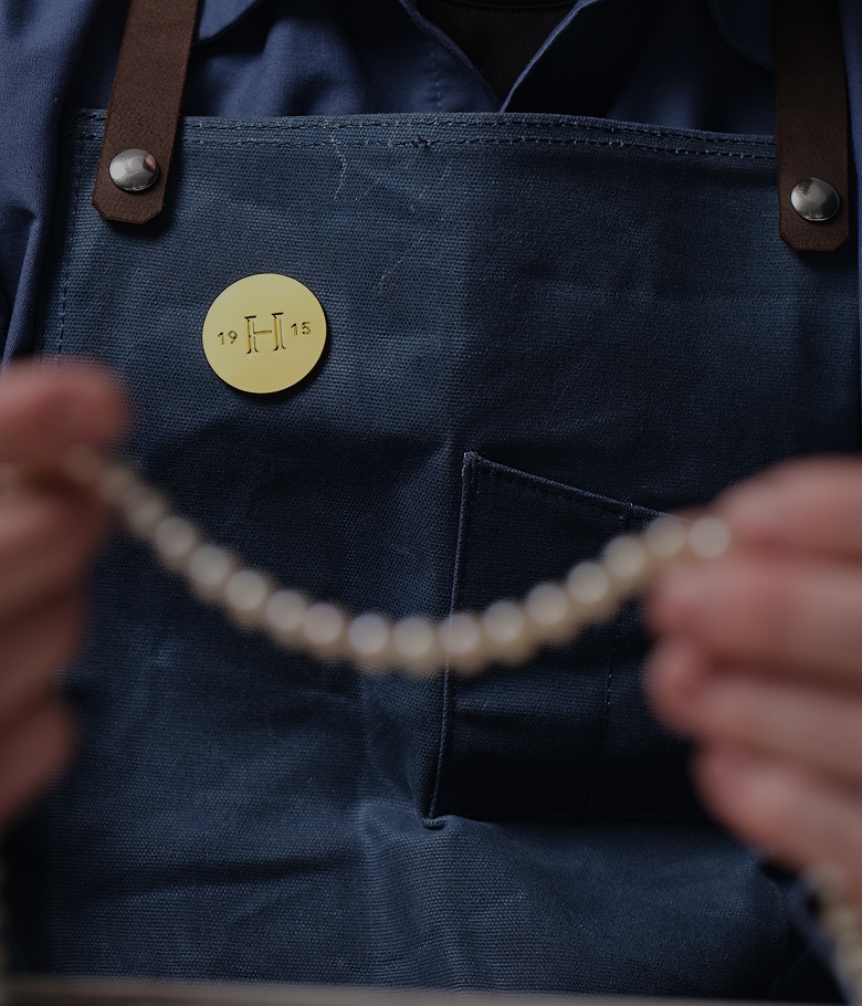 A Helzberg Jeweler holding an out of focus yellow gold necklace
