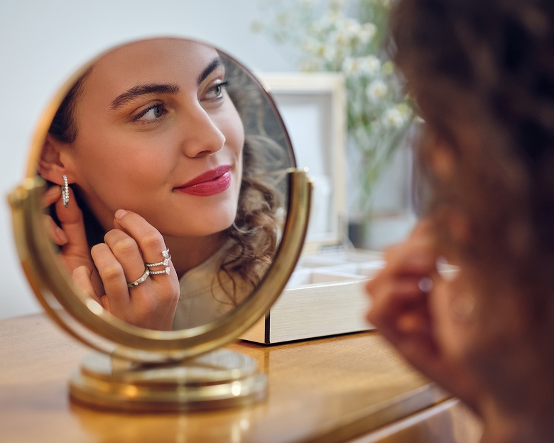 woman putting on lab grown diamond earrings while wearing lab grown diamond rings