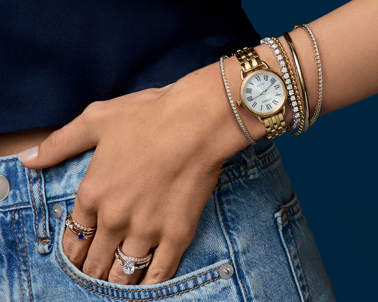 A woman wearing different fashion jewelry bracelets and a watch.