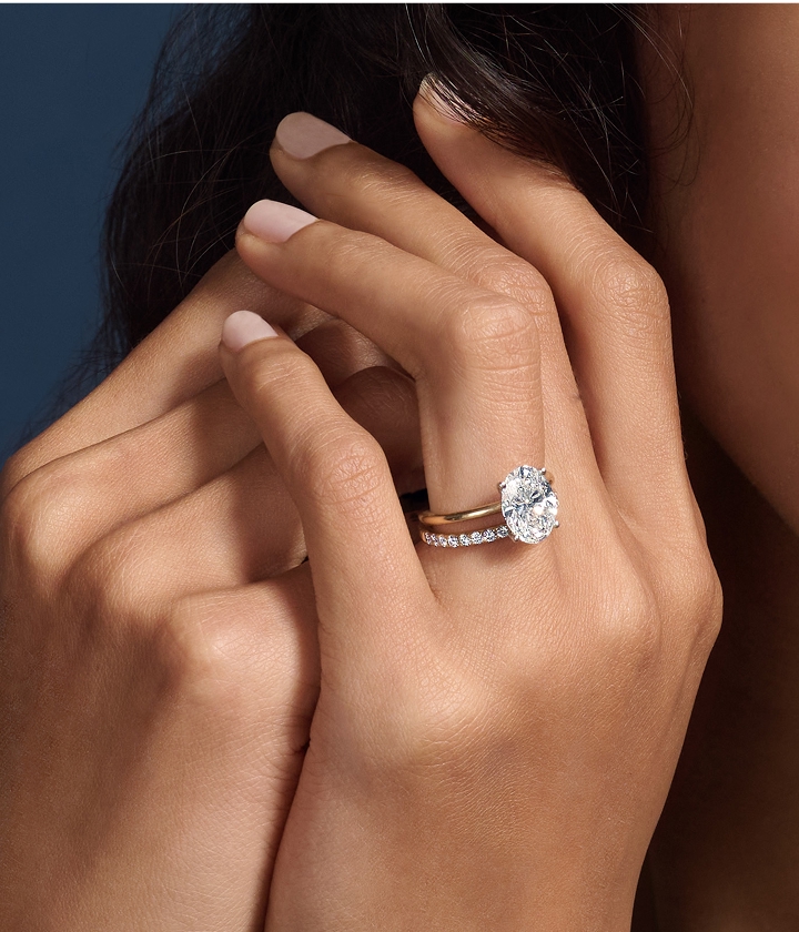 Close up of hand wearing solitaire engagement ring with a gold hand and round diamond paired with a wedding band.