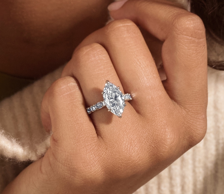 Close-up of a hand wearing a white gold engagement ring with a marquise-cut diamond center stone and a band accented with baguette diamonds.