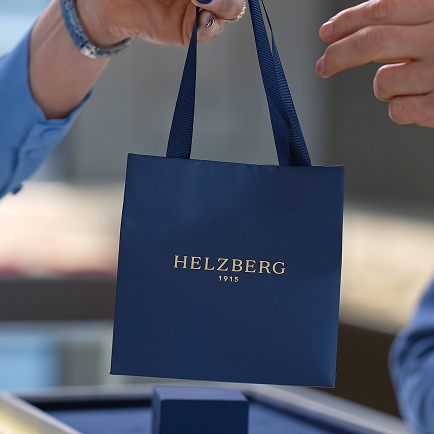 A blue Helzberg shopping bag being passed to the customer above the checkout counter.